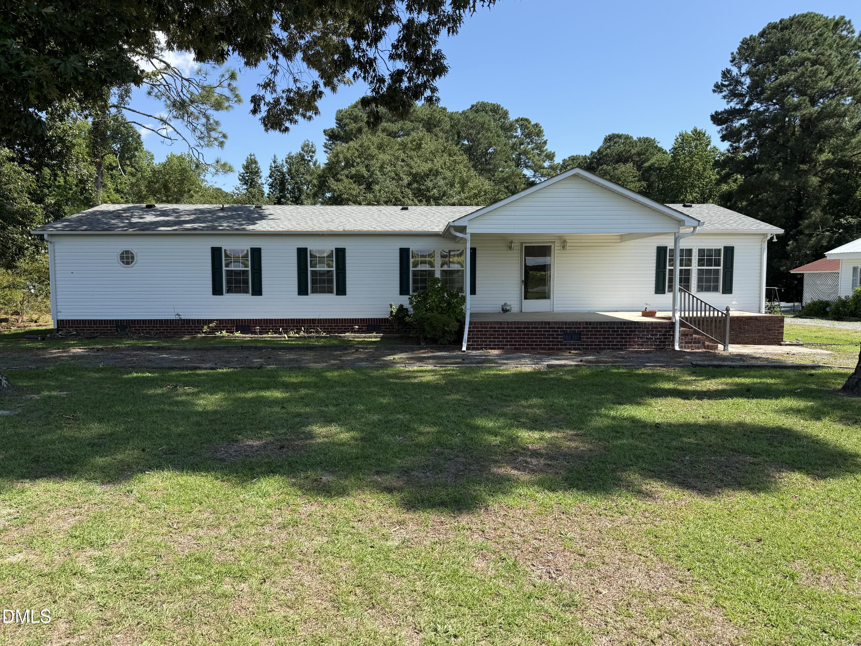 Single-story white house with dark shutters, brick foundation, and a covered front porch.
