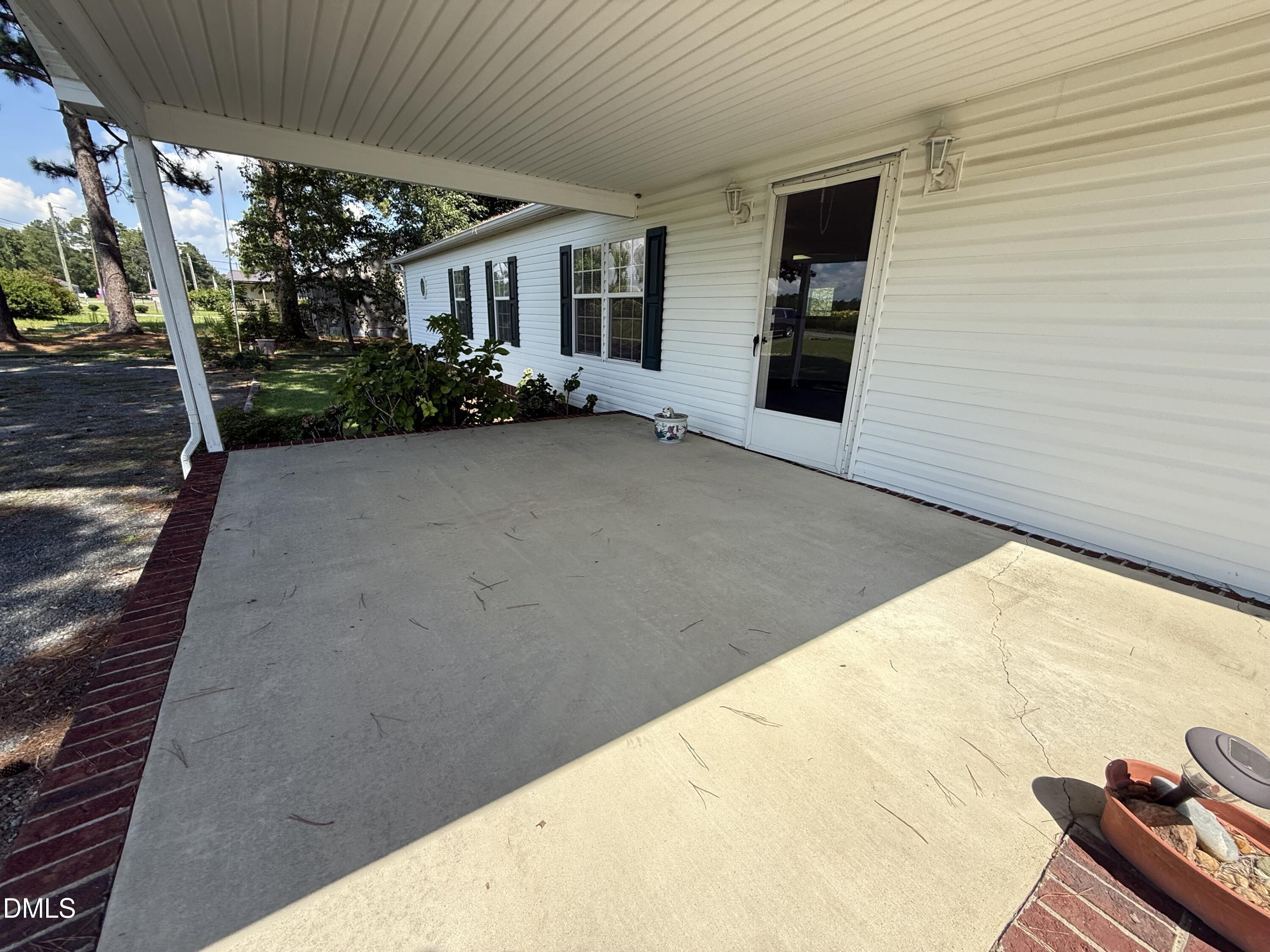 Covered concrete patio beside a white house, with dark shutters and brick edging.