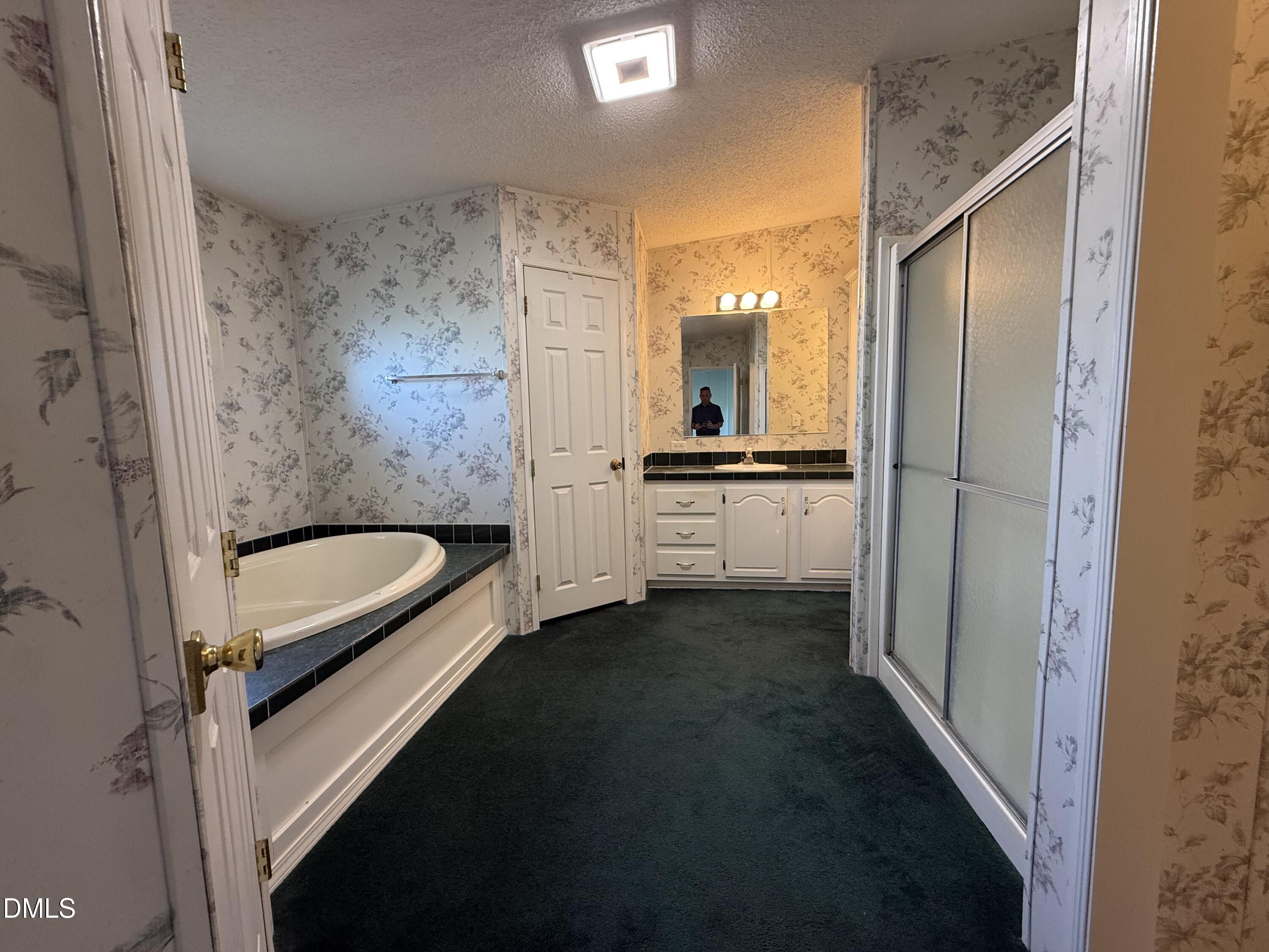 Bathroom with floral wallpaper, a built-in soaking tub, white vanity, and frosted-glass shower.