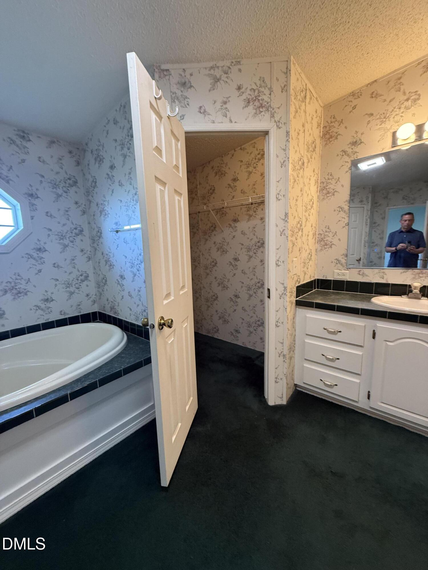 Bathroom with a corner bathtub, floral wallpaper, black tile, and a white vanity.