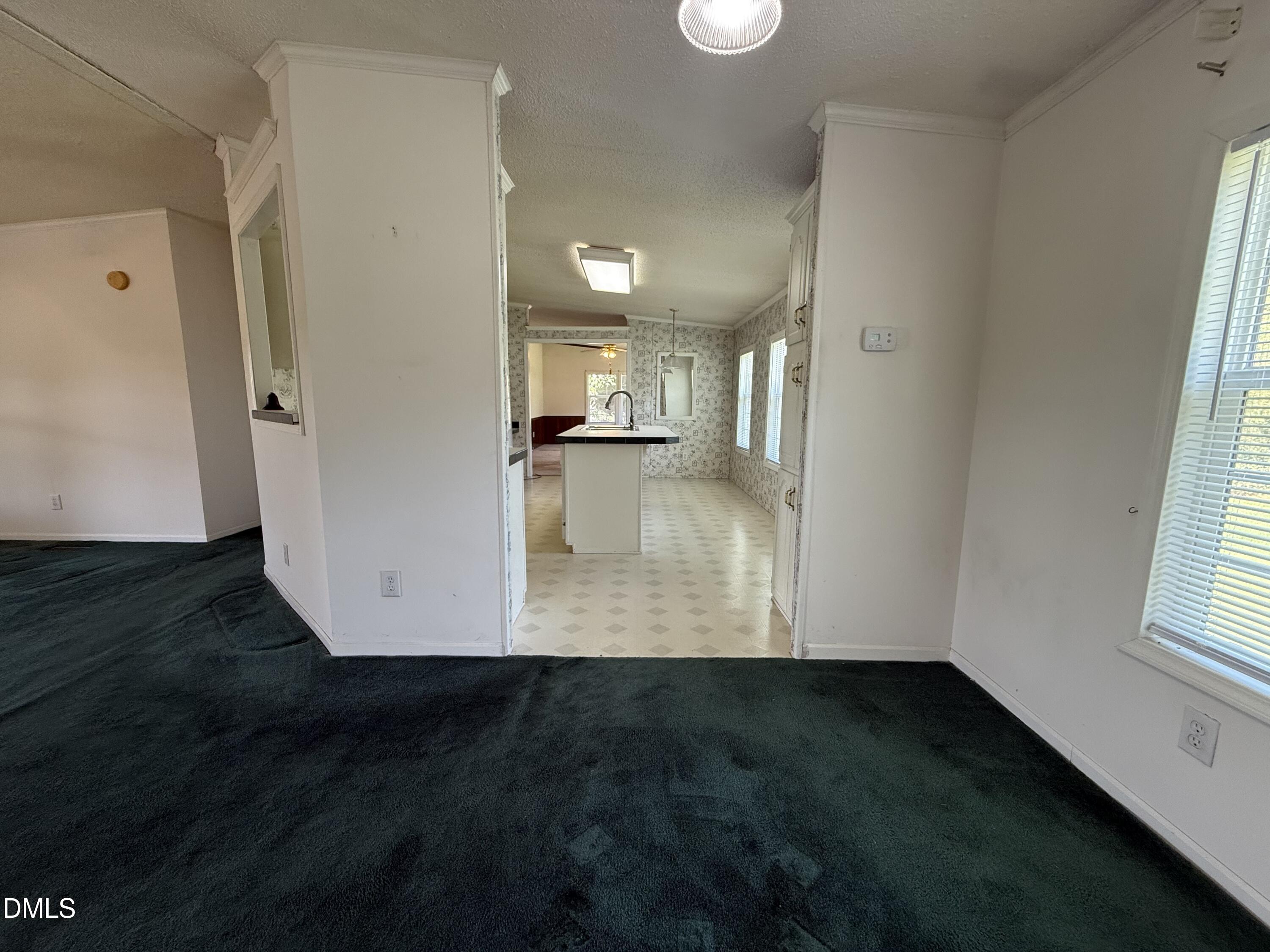 Unfurnished living room with dark teal carpet opening onto a kitchen with a central island.