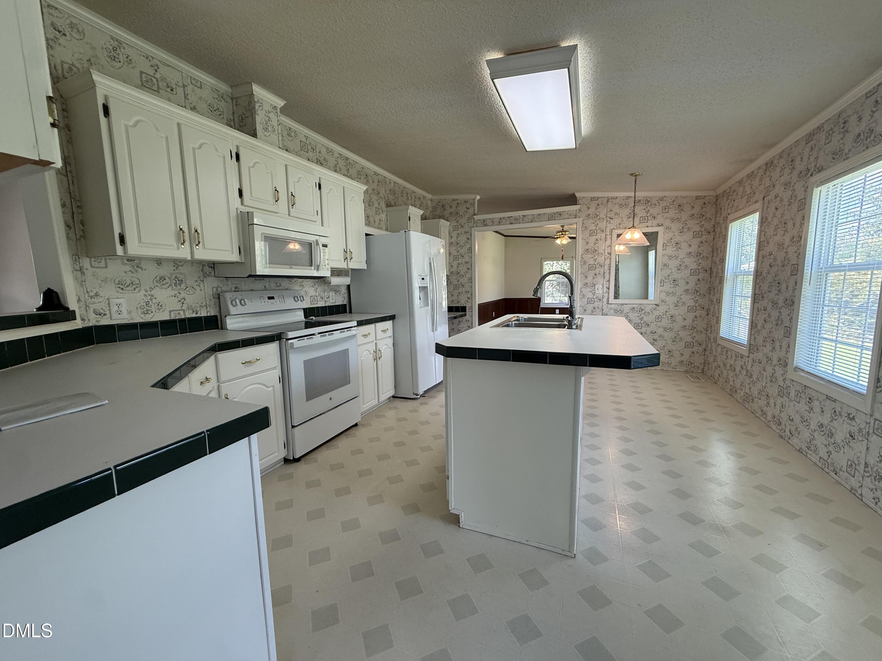 Kitchen with white cabinets and appliances, a large island sink, and patterned wallpaper.