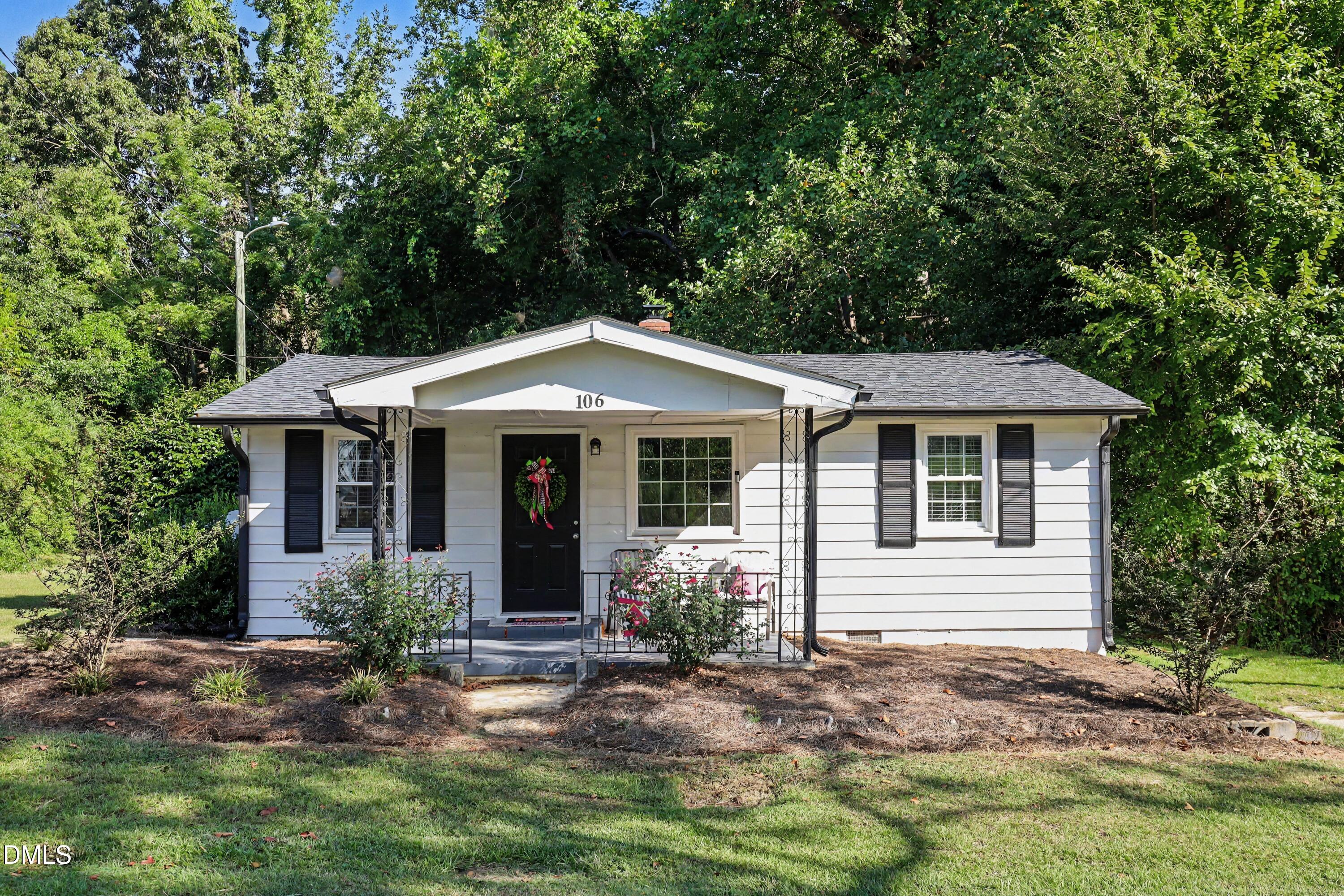White single-story house with black shutters, covered porch, and wreath on the front door.