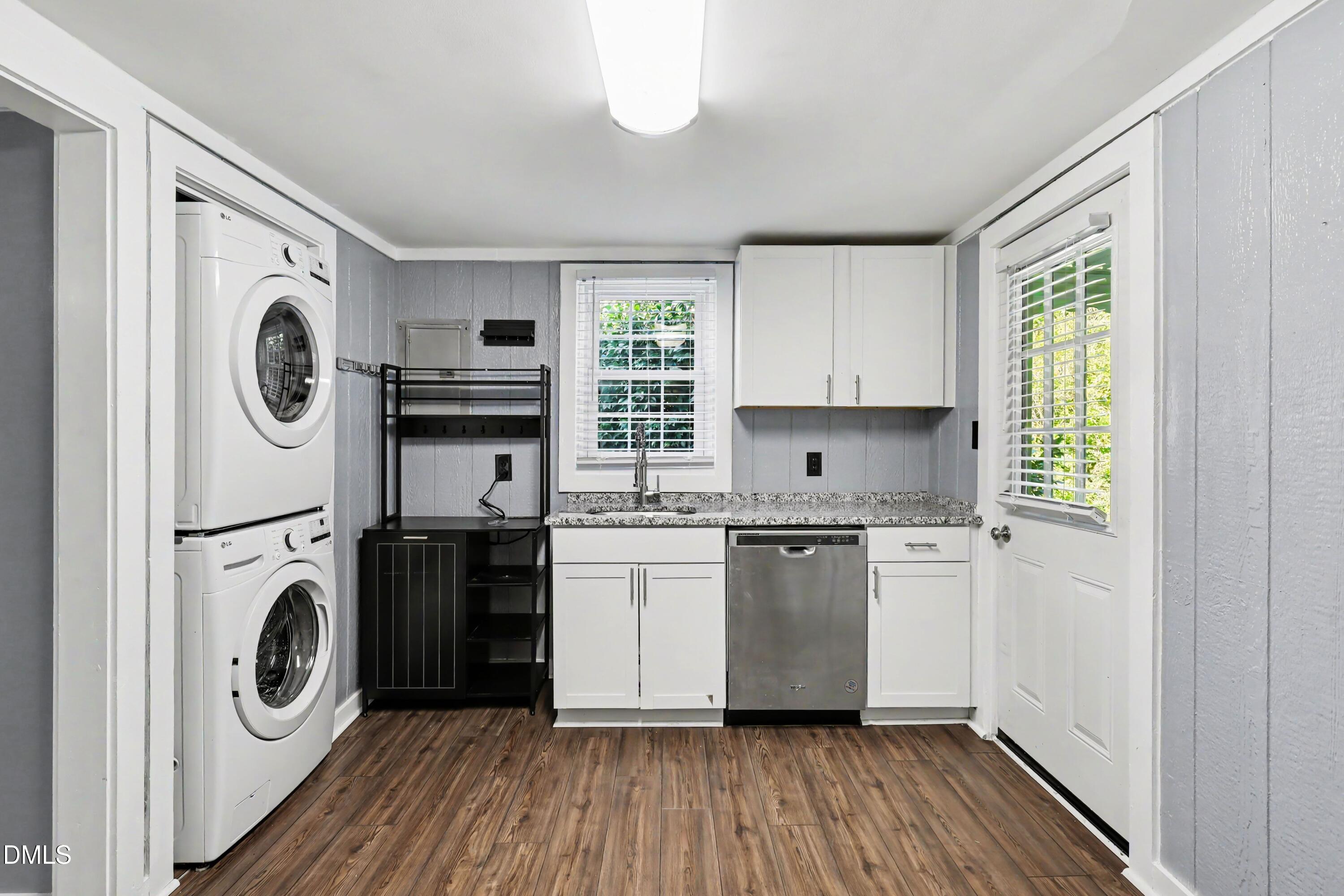 Laundry room with stacked washer and dryer, white cabinets, sink, and stainless-steel dishwasher.