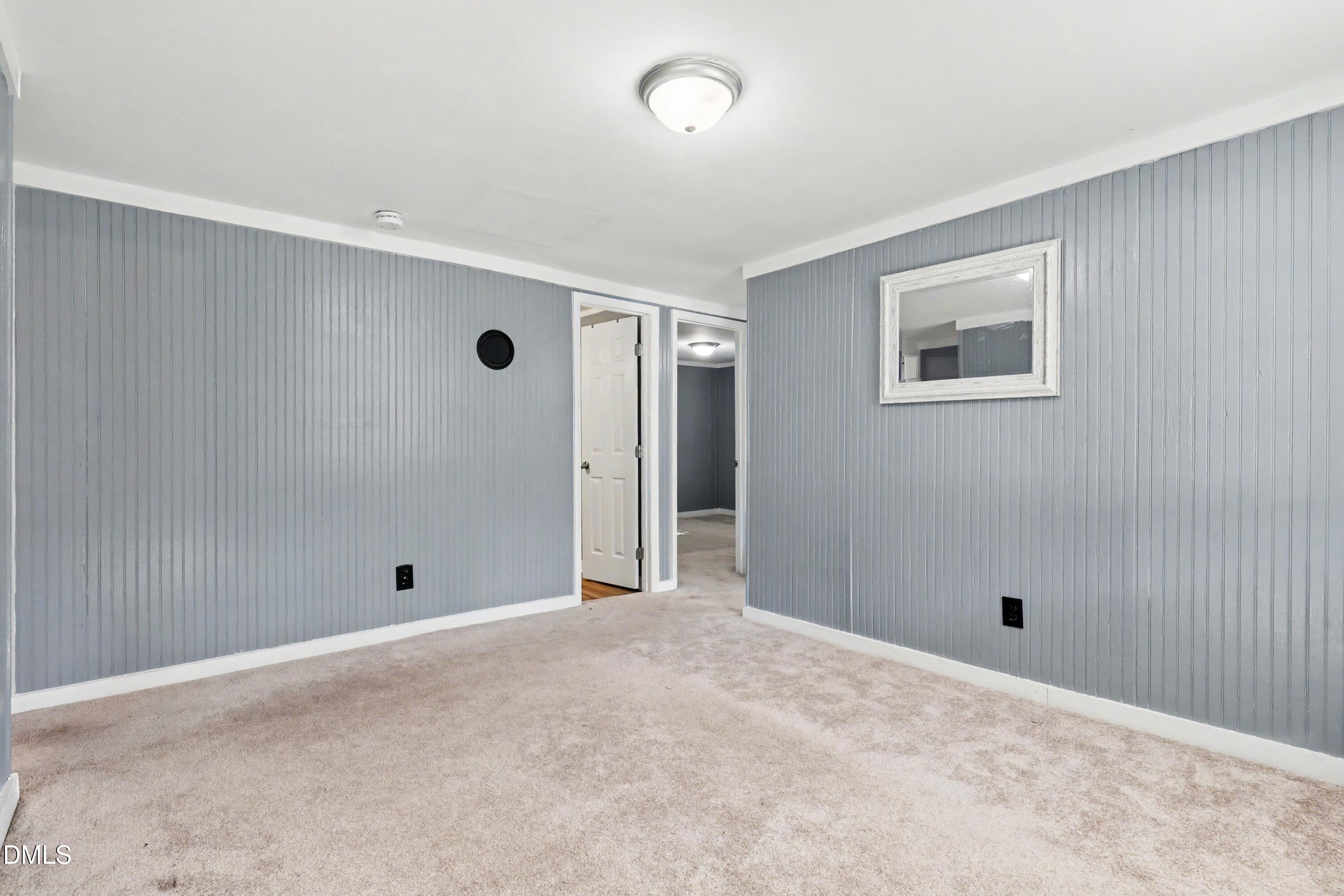 Empty room with gray paneled walls, beige carpet, and a framed mirror.