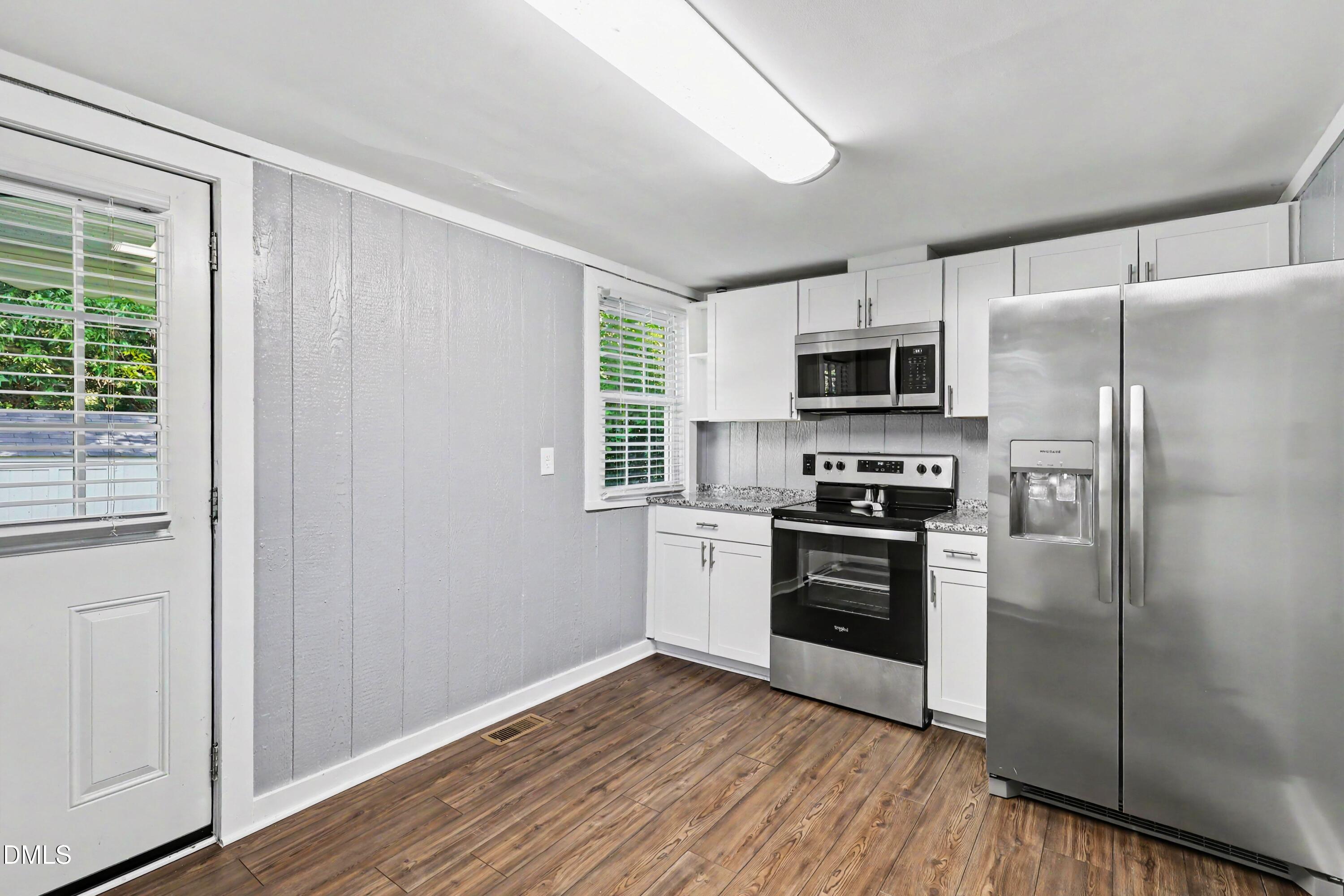 Kitchen with white cabinets, stainless steel appliances, and wood-look plank flooring.