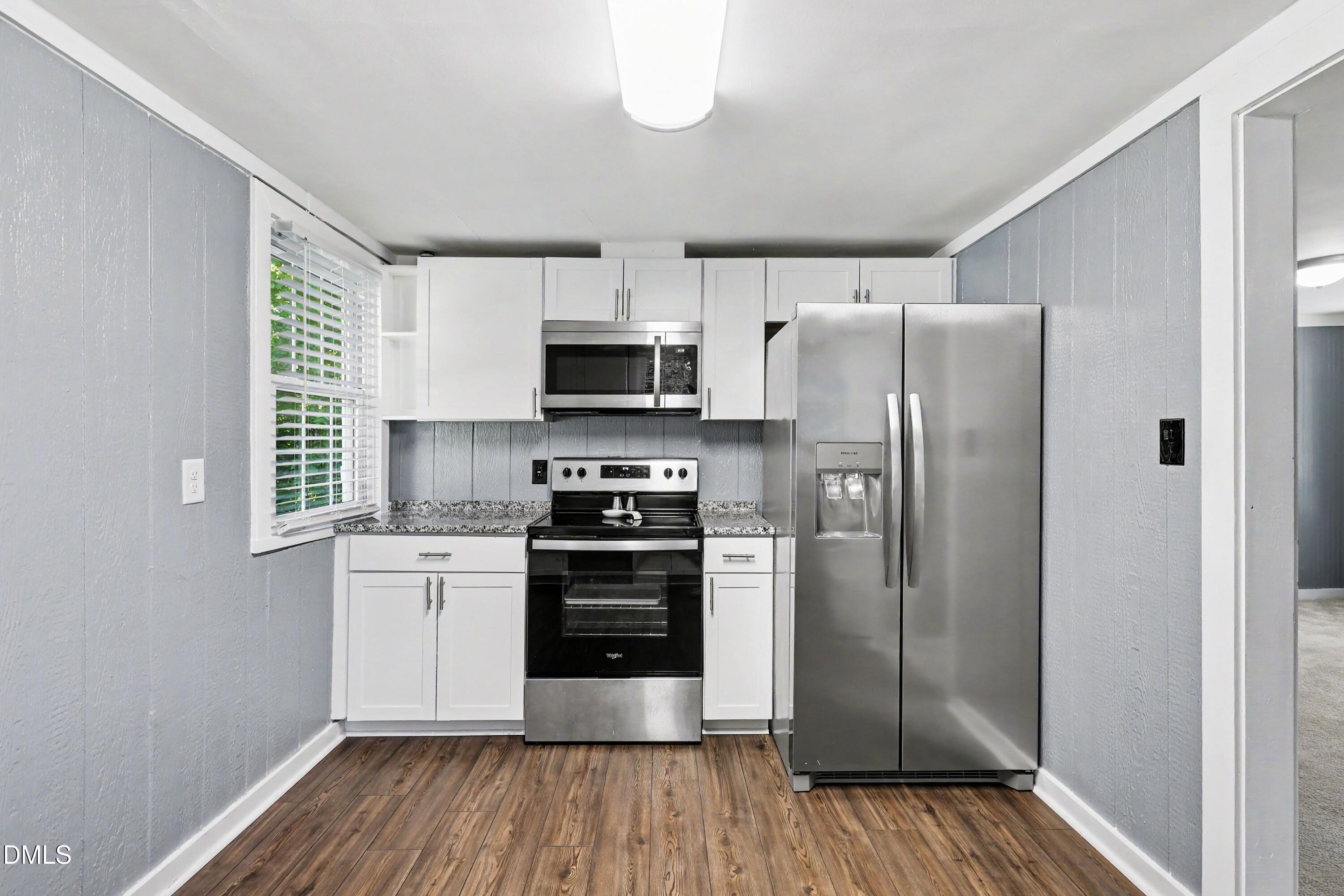 Kitchen with white cabinetry, stainless steel appliances, and wood-look flooring.