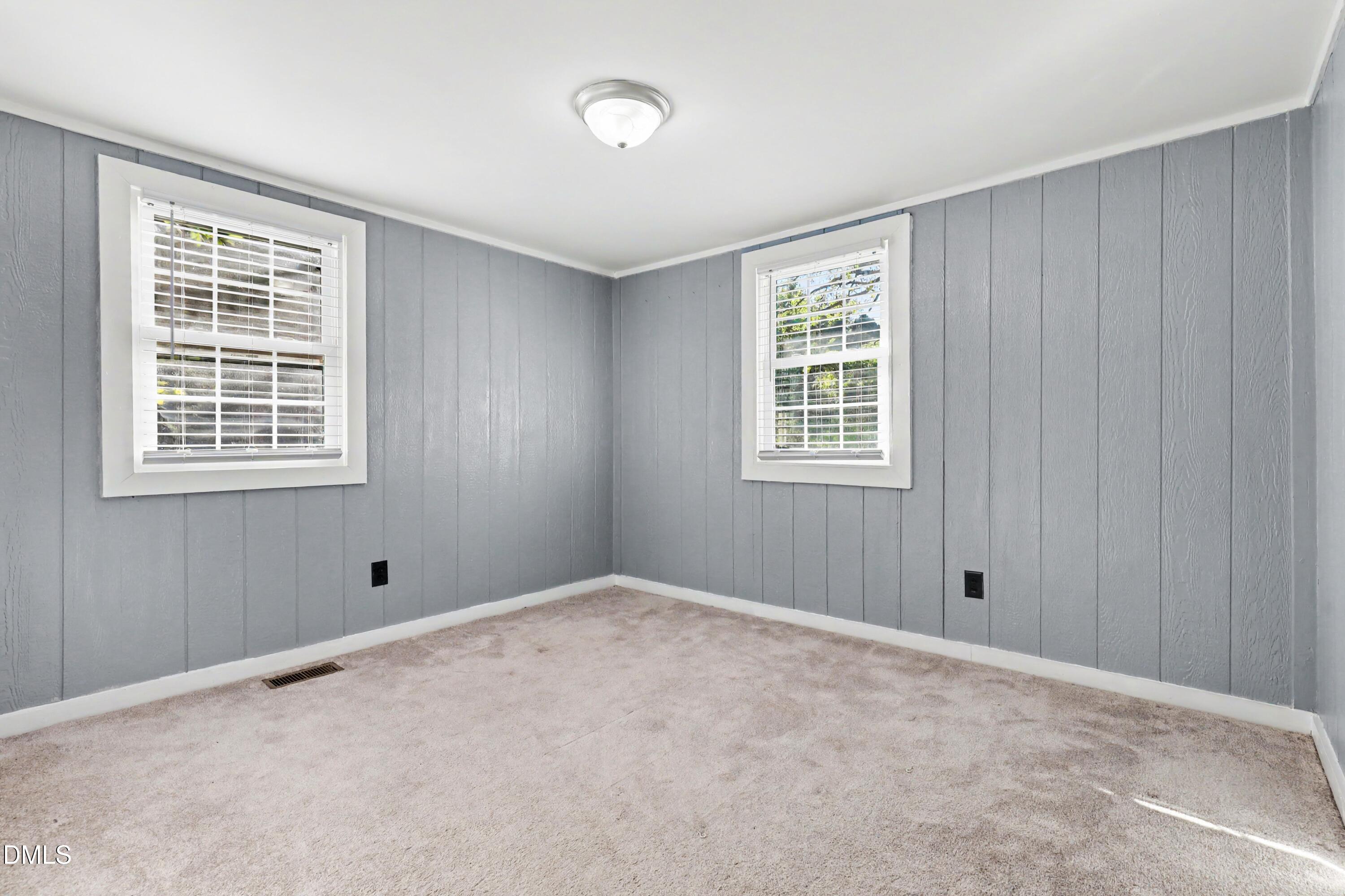 Vacant carpeted room with gray paneled walls and two windows with white blinds.