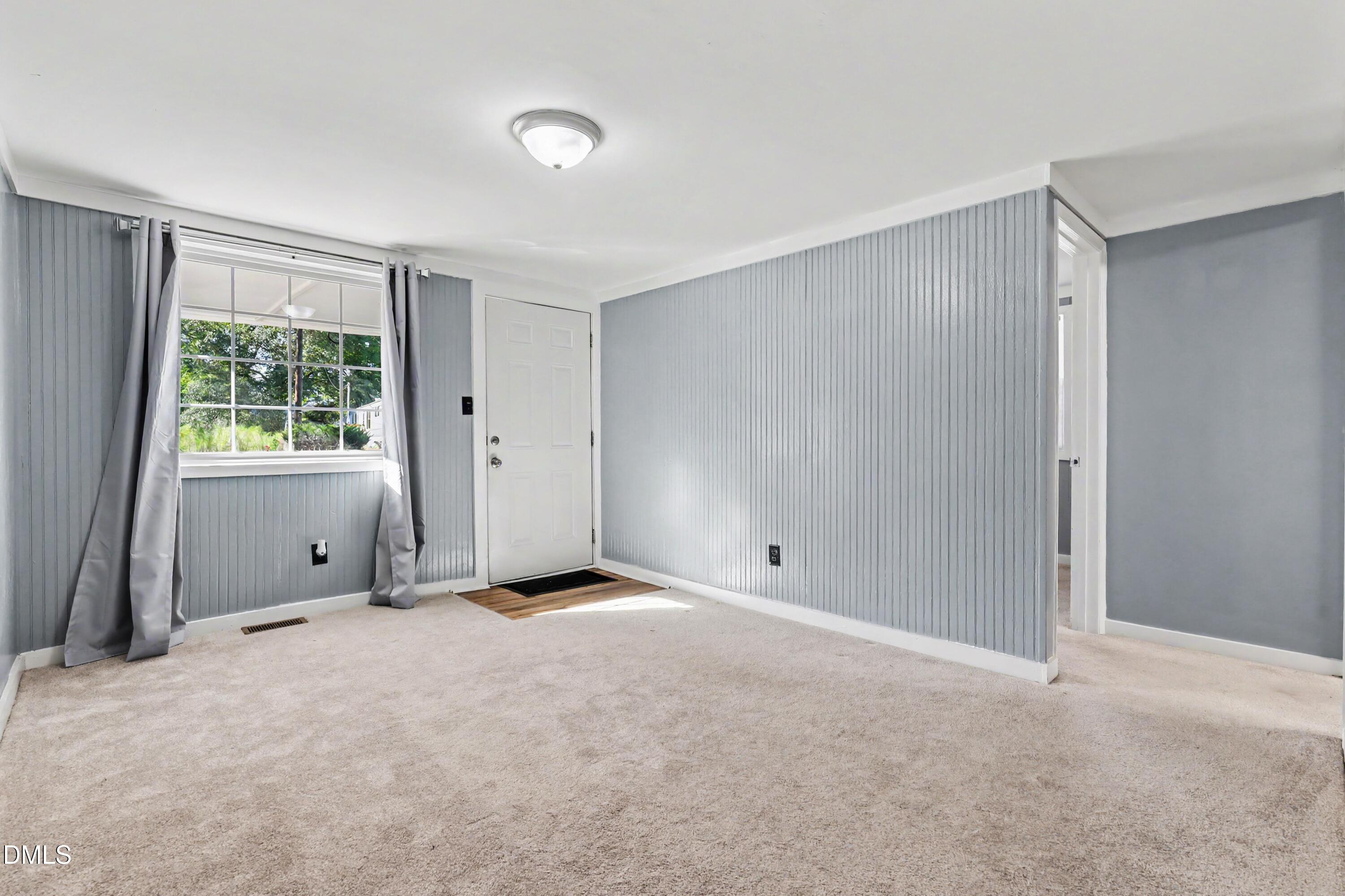 Vacant entry room with gray paneled walls, a curtained window, and a white front door.