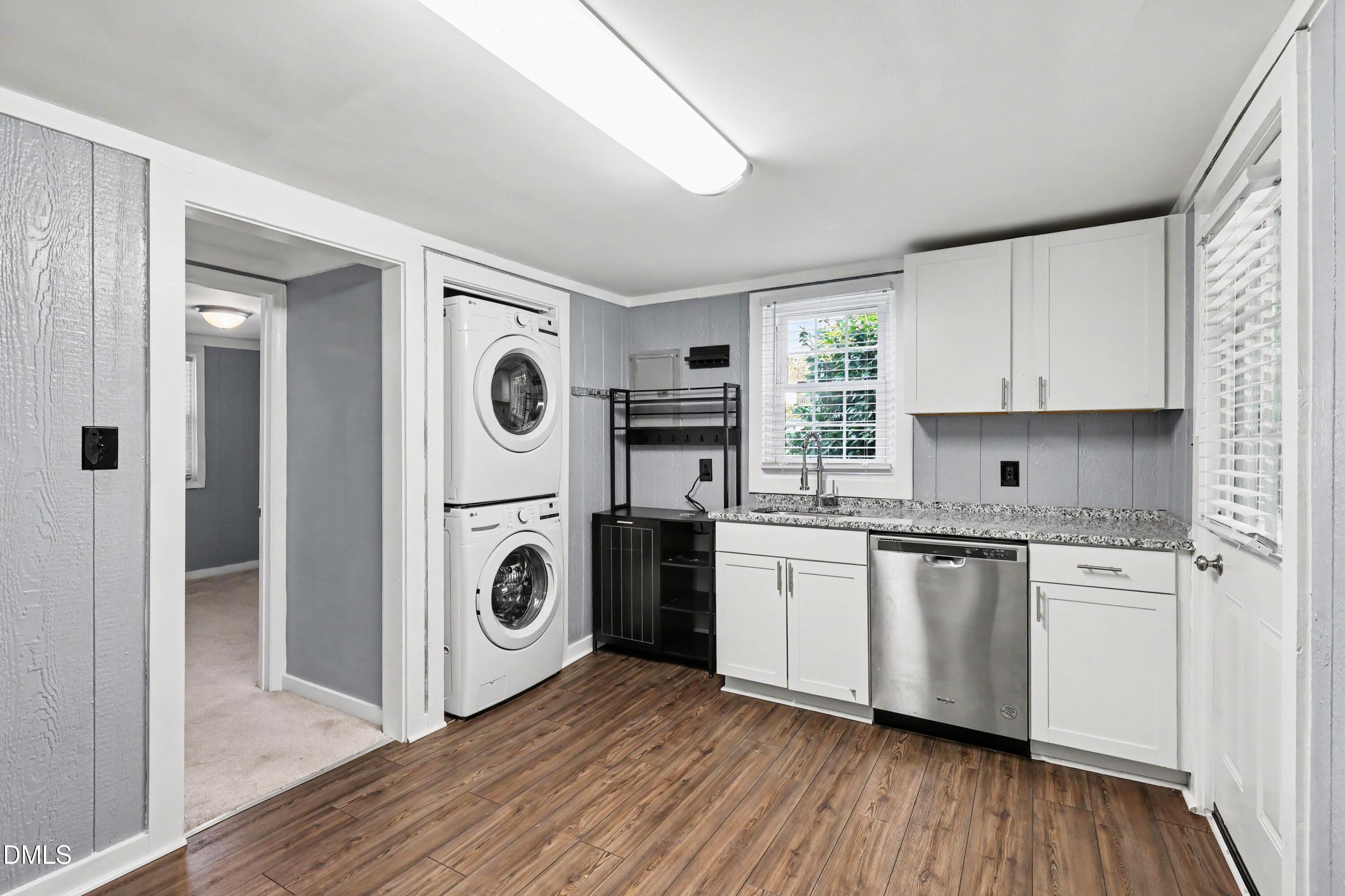 Laundry room with stacked washer and dryer, white cabinets, granite counter, and stainless-steel dishwasher.
