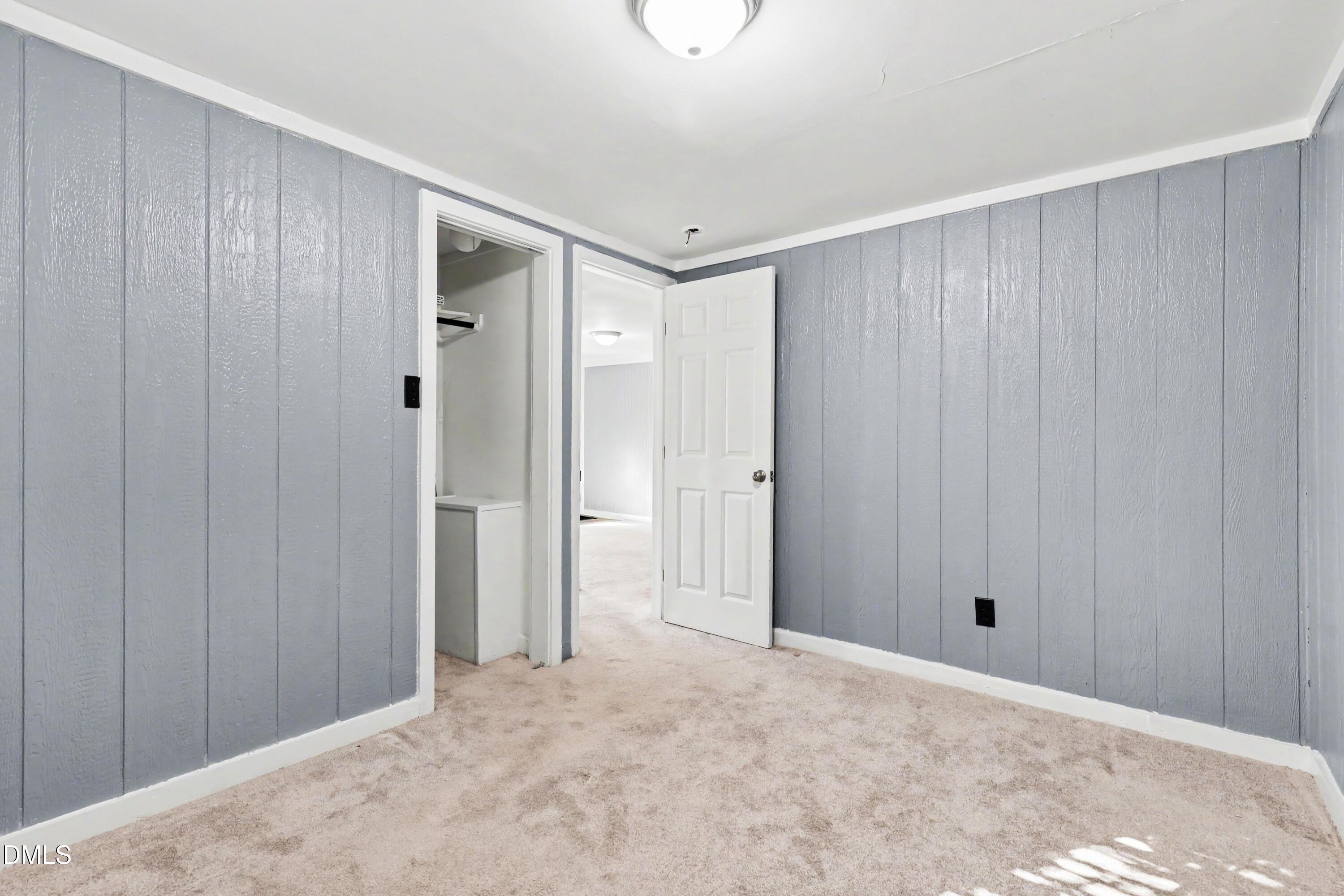 Unfurnished room with gray paneled walls, beige carpet, and an open closet beside the doorway.