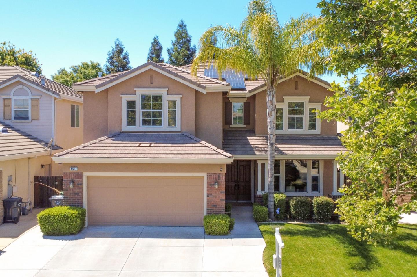Two-story tan home with solar panels, a double garage, and a landscaped front yard.