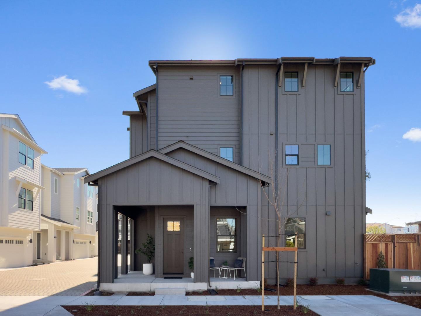 Gray three-story modern home with a covered entry and small patio seating.