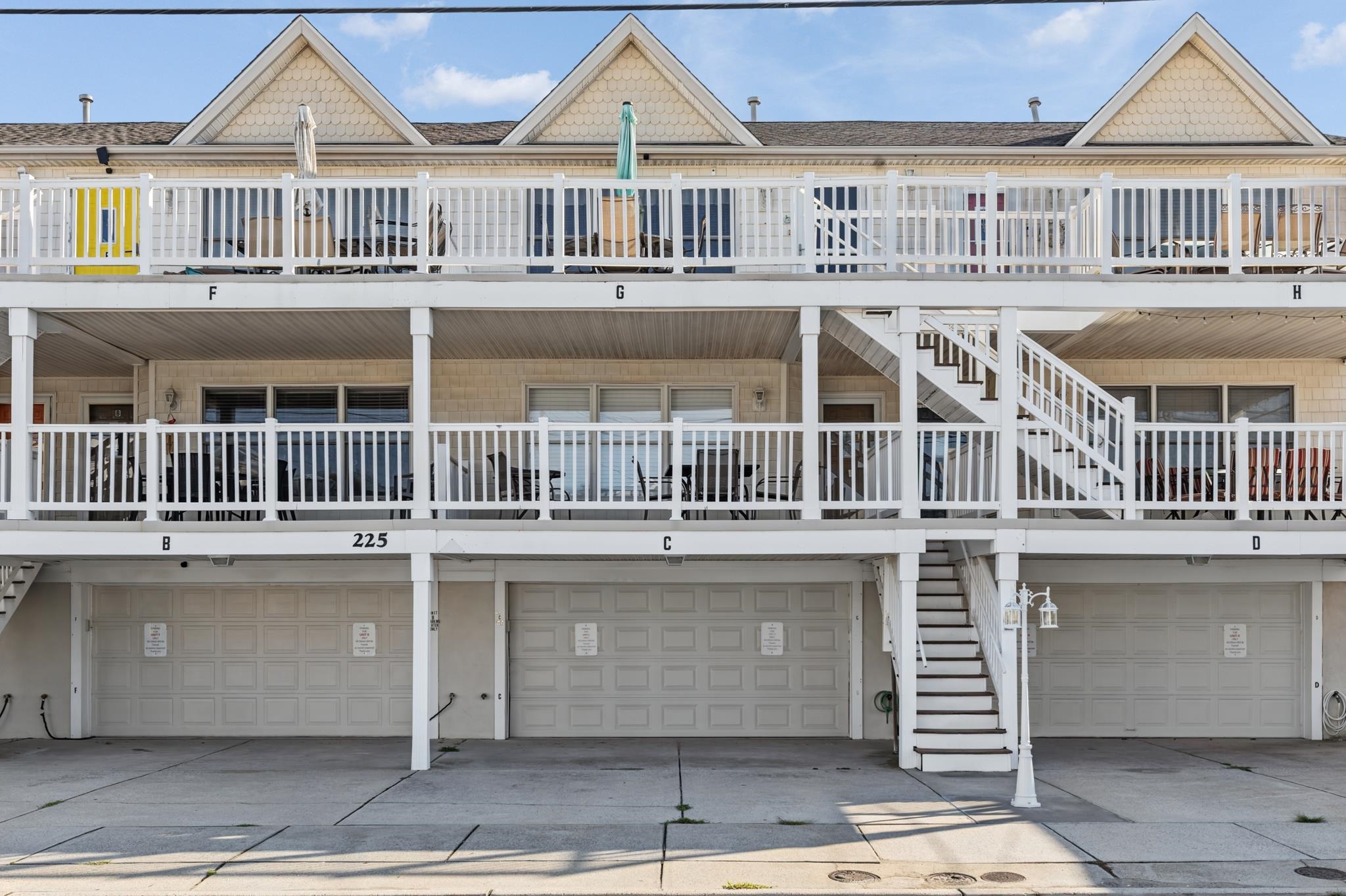 Multi-level coastal building with white balconies, exterior stairs, and ground-floor garages.