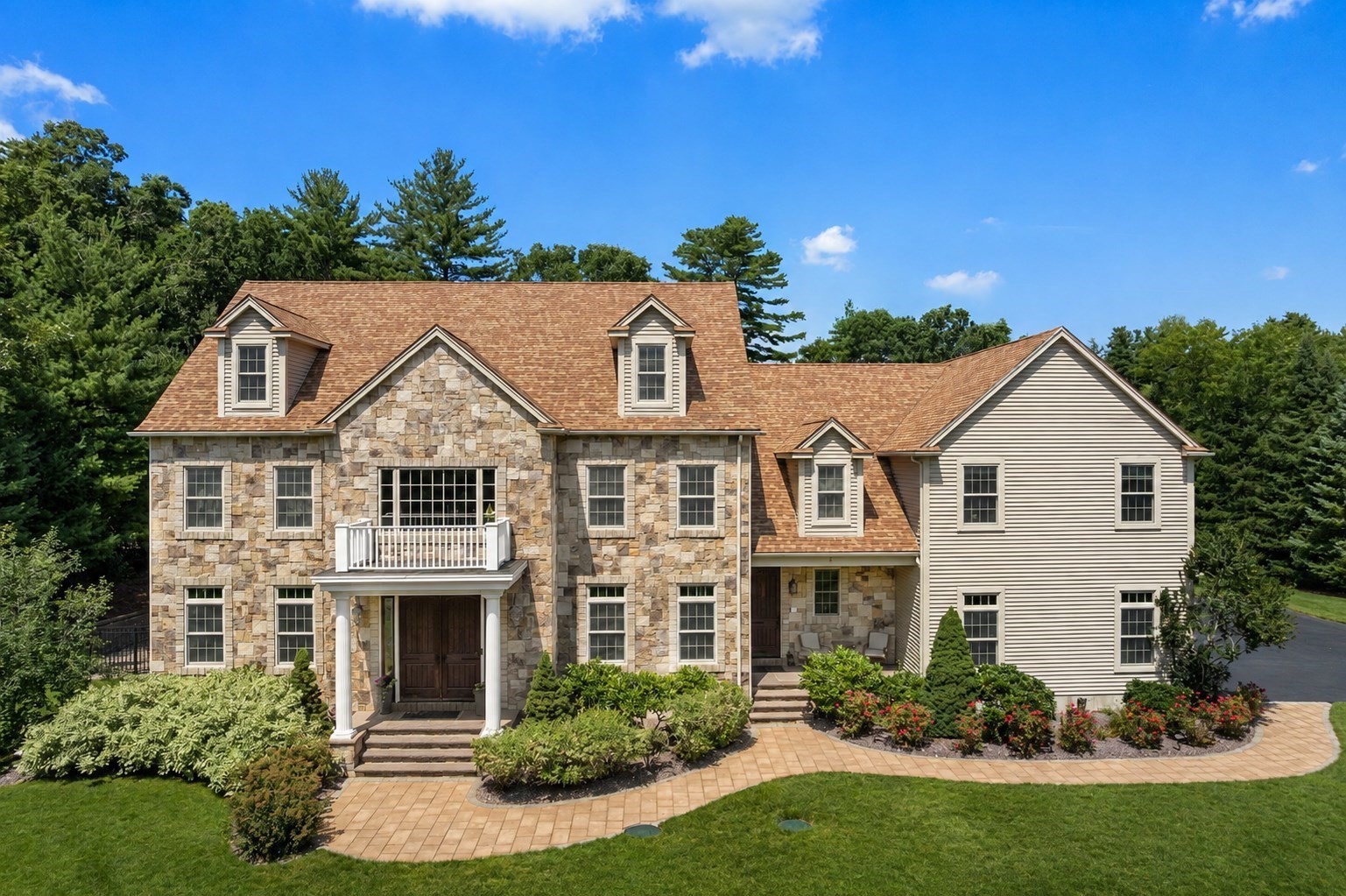 Large stone-and-siding home with dormers, a front balcony, and landscaped gardens.