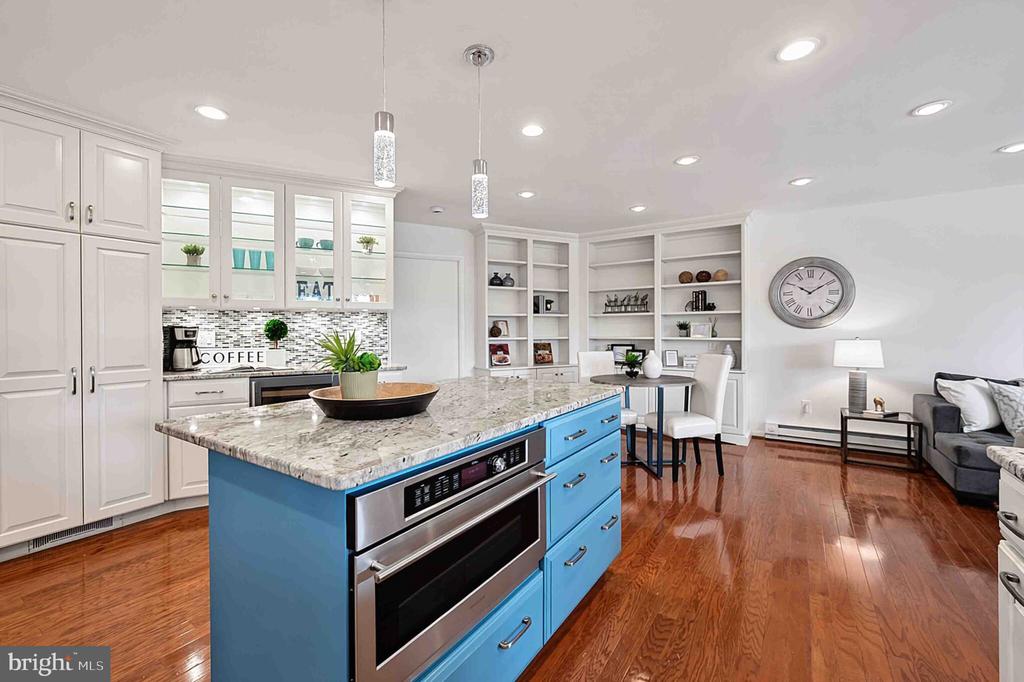 Open-plan kitchen with a blue island, marble-pattern counter, white cabinetry, and hardwood floors.