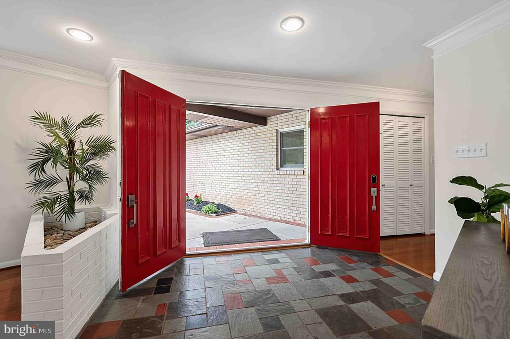 Entry foyer with open red double doors, multicolored slate flooring, and a built-in planter.