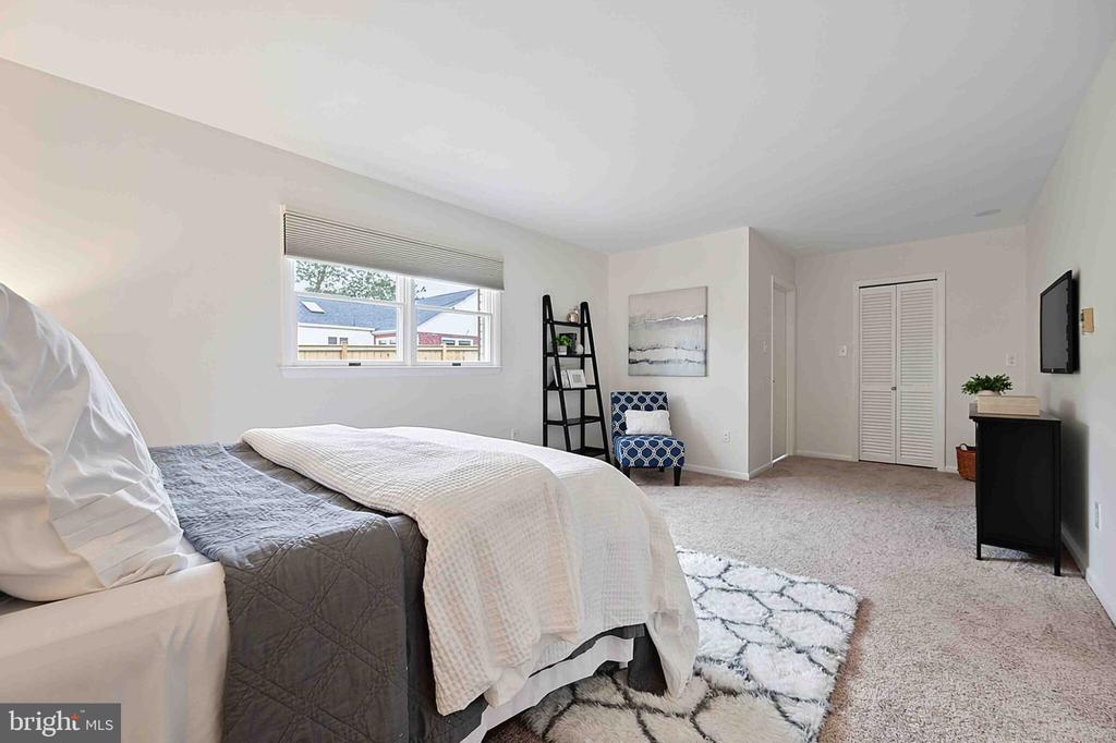 Staged bedroom with gray and white bedding, a blue accent chair, and a patterned rug.