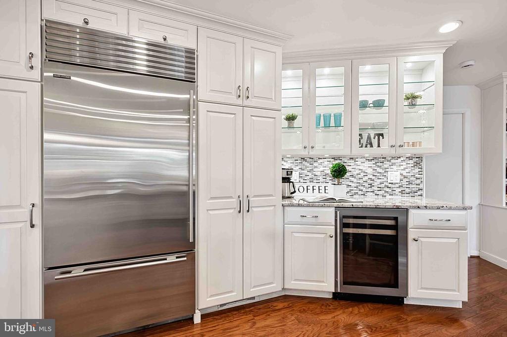 White kitchen with a large stainless-steel refrigerator, glass-front cabinets, and a mosaic backsplash.