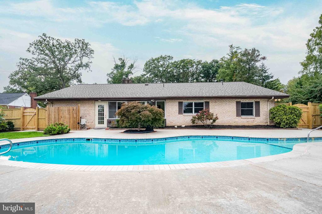 Backyard swimming pool in front of a single-story brick home and fenced patio.