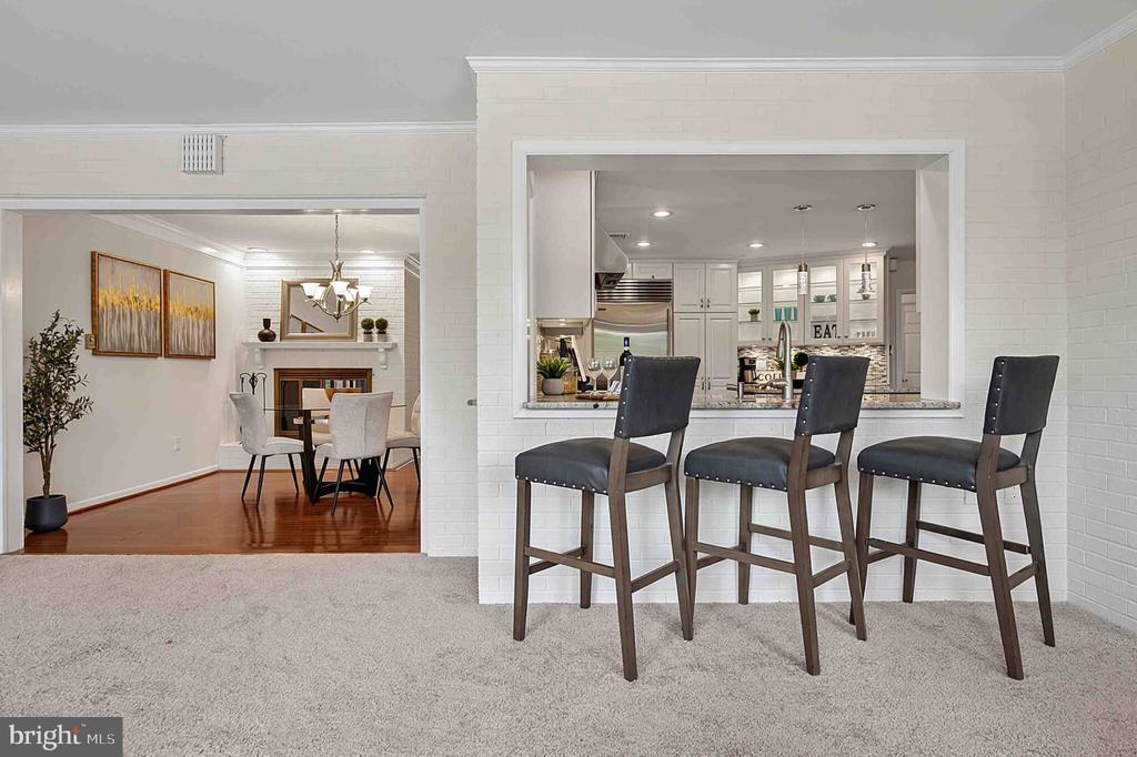Kitchen pass-through with three dark bar stools opens onto a dining room with a fireplace.