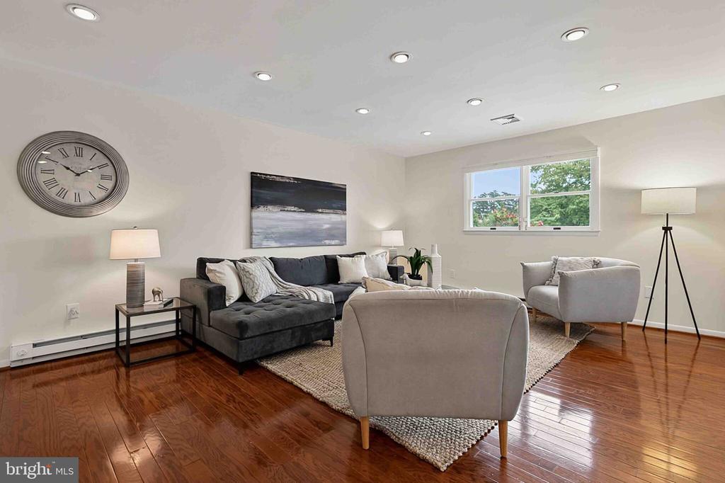 Living room with a gray sectional, light chairs, hardwood floors, and a window overlooking greenery.