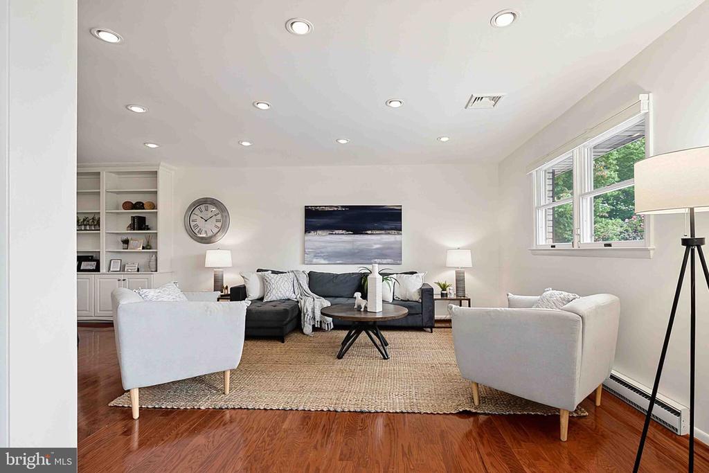 Staged living room with a dark sofa, white armchairs, built-in shelves, and hardwood floors.