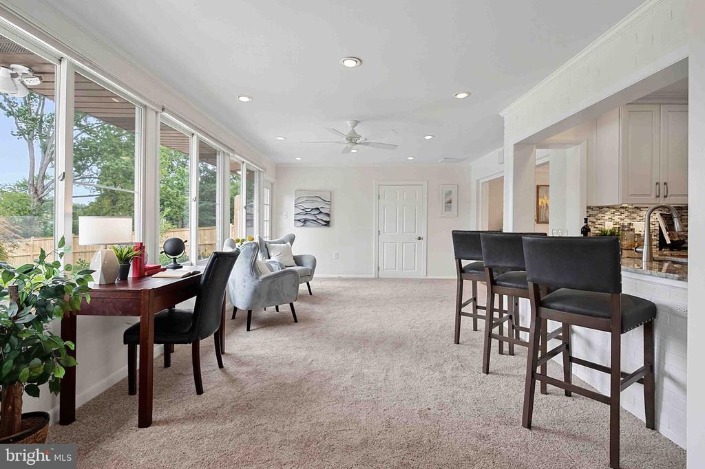 Furnished living and dining area with a desk beside broad windows and a kitchen breakfast bar.