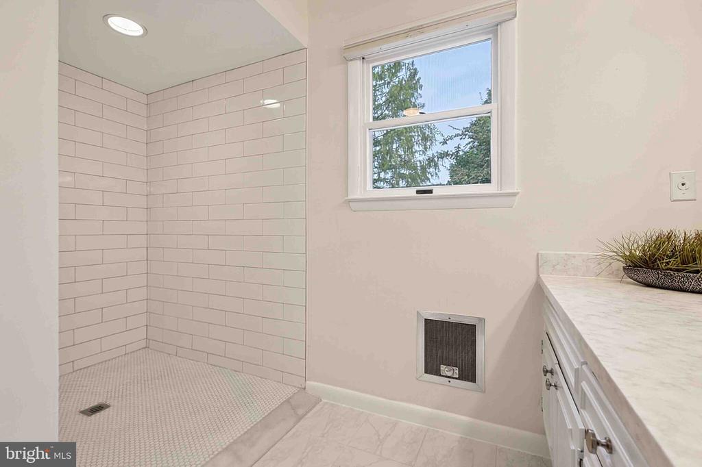Bathroom with a white subway-tile shower, mosaic floor, and marble-look vanity beside a window.
