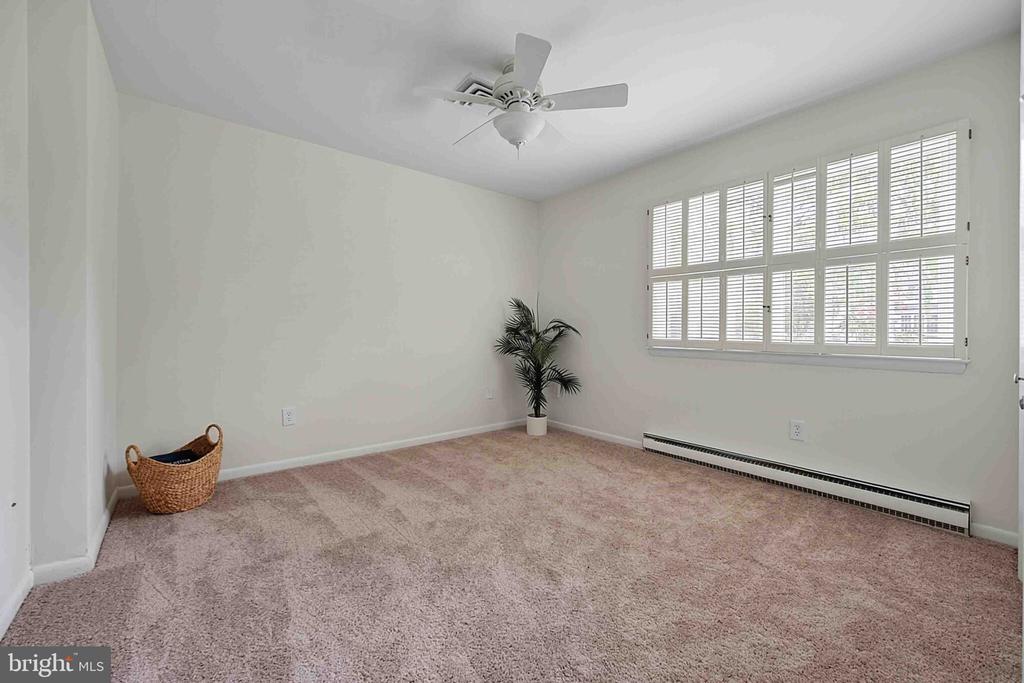 Carpeted room with plantation-shuttered windows, a ceiling fan, and a long baseboard heater.