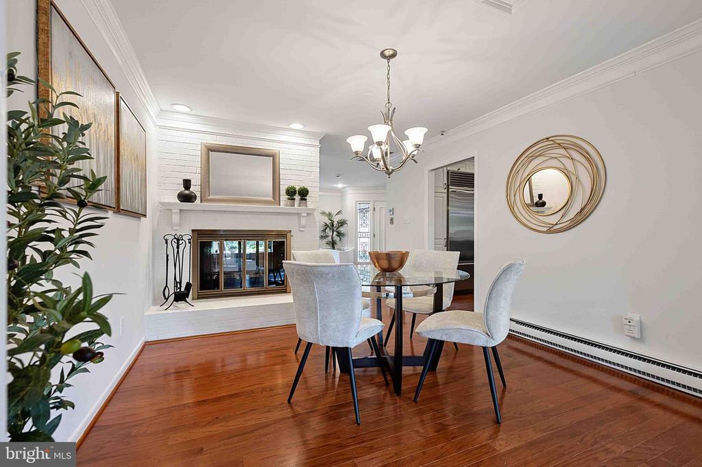 Dining room with a glass-top table, hardwood floors, and a white brick fireplace.
