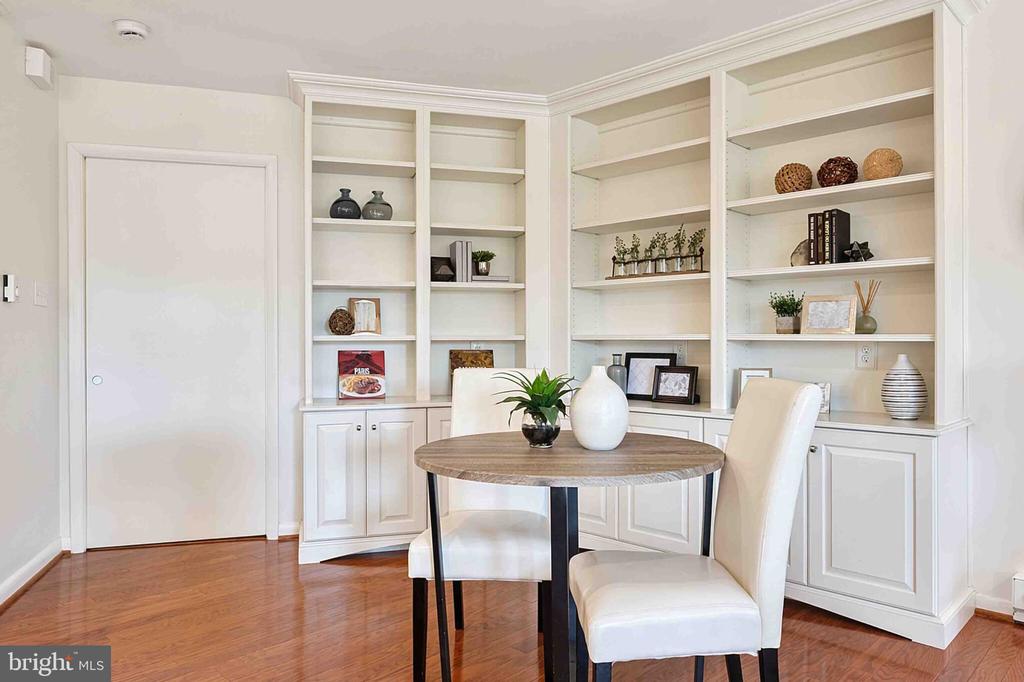 Staged sitting area with white built-in bookshelves, a round table, and two upholstered chairs.