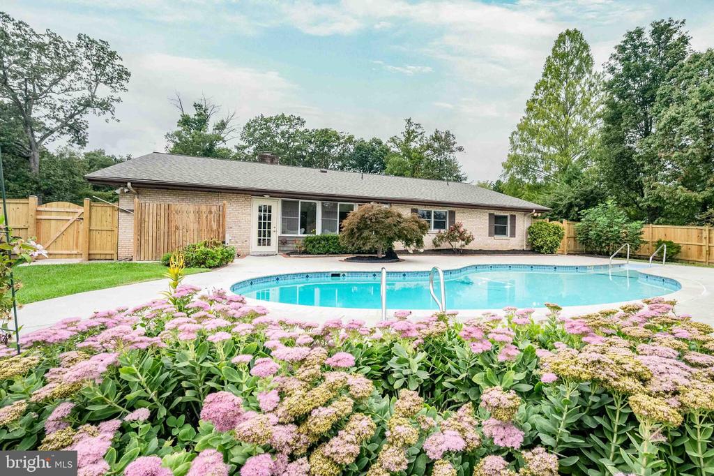 Brick home behind a swimming pool, with wooden fencing and pink flowers in the foreground.