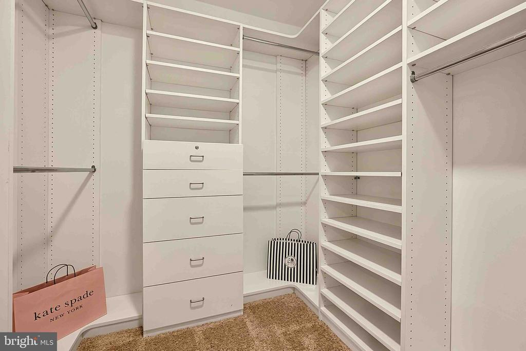 Walk-in closet with white built-in shelves, central drawers, and handbags on the lower shelves.