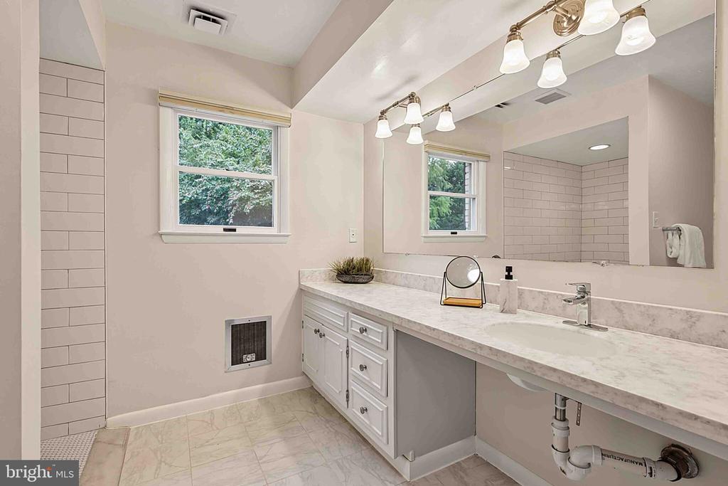 Bathroom with a long white vanity, marble-look counter, large mirror, and two windows.