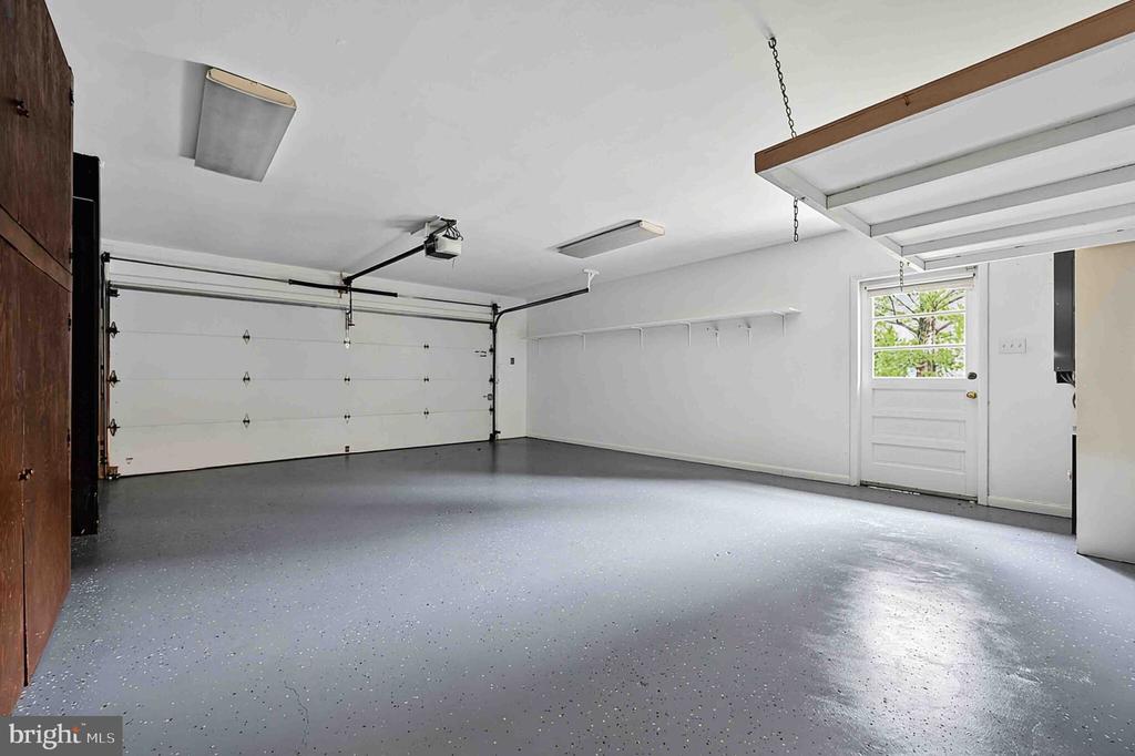 Empty garage with a gray speckled floor, wide overhead door, and side entry door.