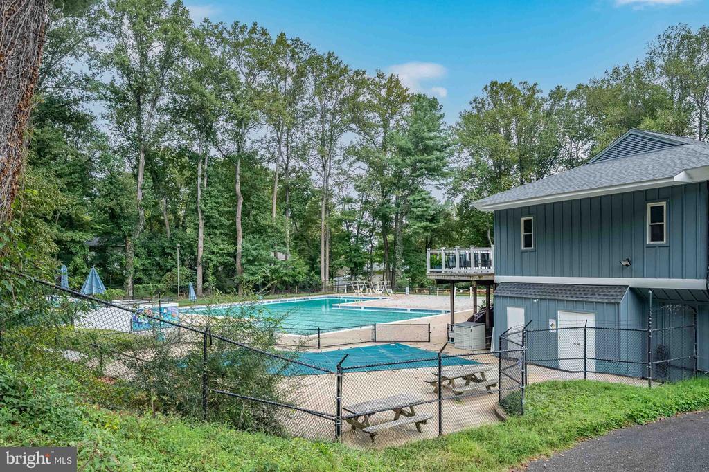 Outdoor swimming pool with a fenced deck, picnic tables, and a blue-sided pool building.