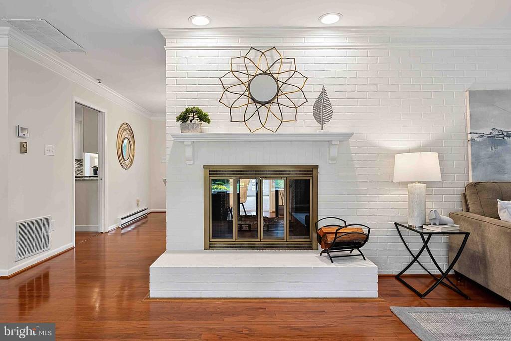 Staged living room with a white brick fireplace, brass-framed doors, and hardwood floors.