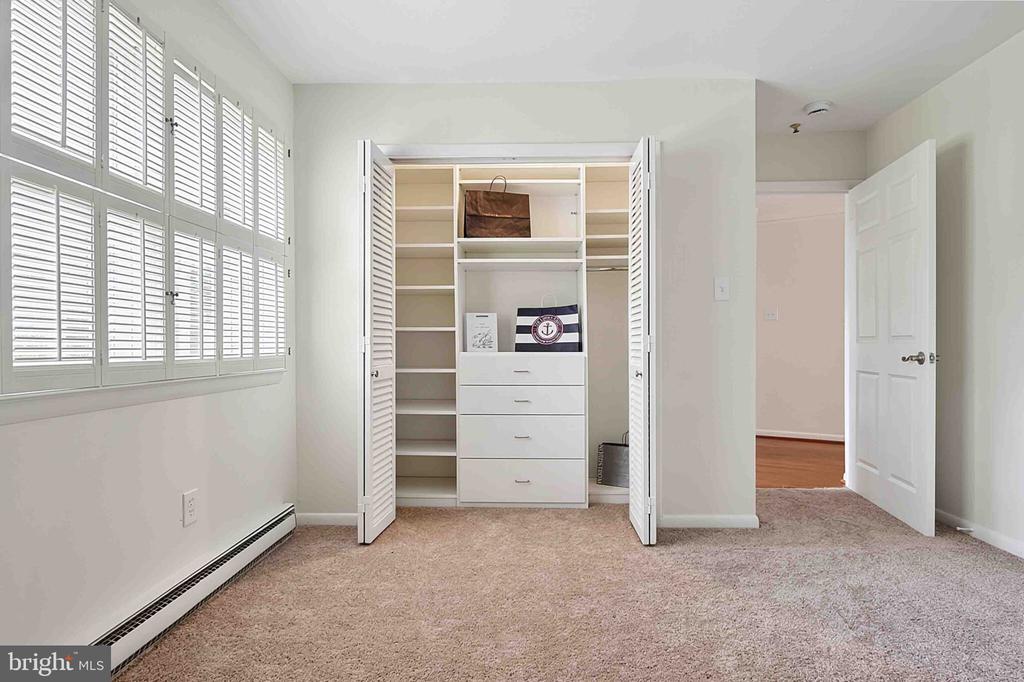 Carpeted bedroom with shuttered windows and an open closet with built-in shelves and drawers.