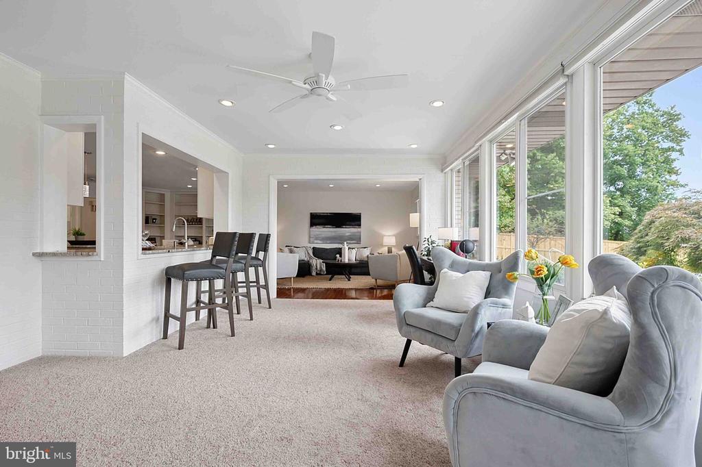 Bright carpeted living area with gray armchairs, large windows, and a breakfast bar opening to the kitchen.