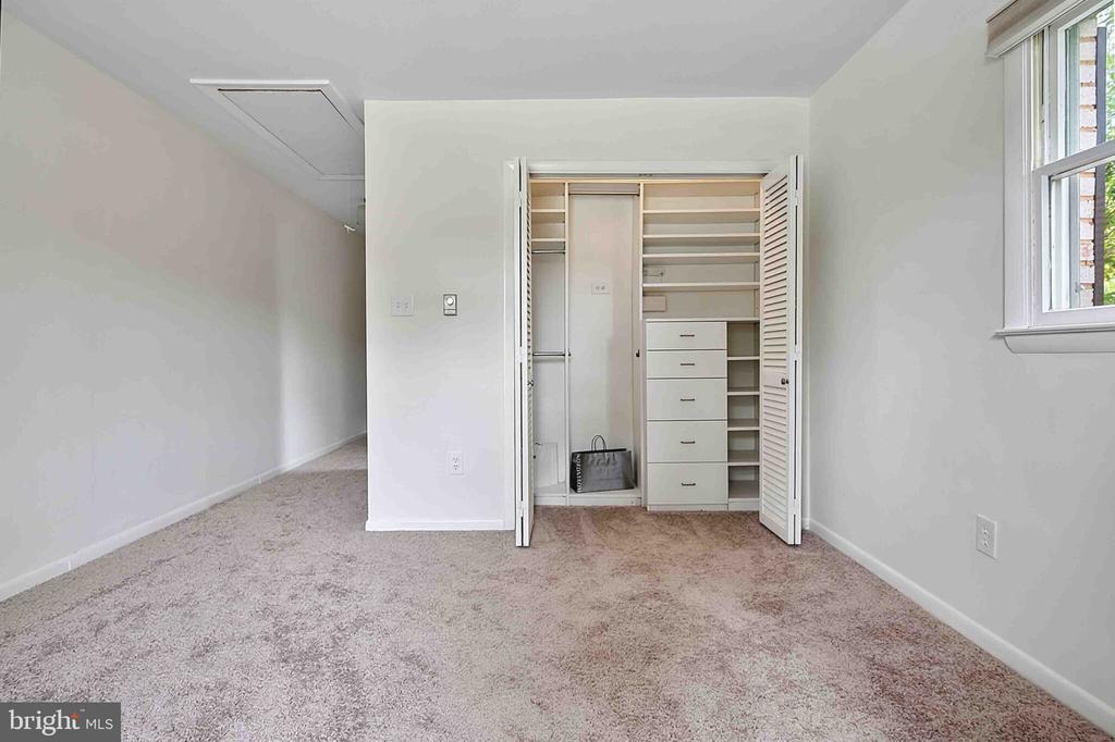Empty carpeted bedroom with an open built-in closet featuring shelves and drawers.