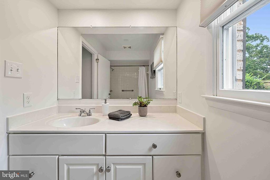 Bathroom vanity with gray cabinets, a large mirror, and a window overlooking trees.