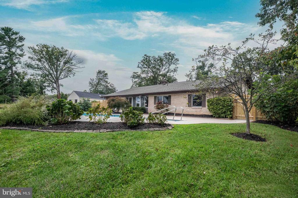 Brick home with a backyard swimming pool, green lawn, mature trees, and fenced yard.