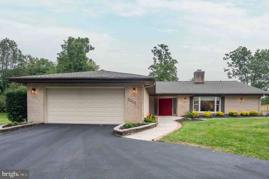 Single-story brick home with a red front door, attached garage, and broad paved driveway.