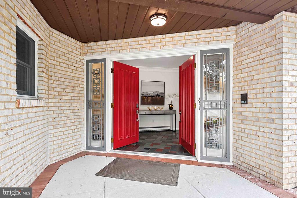 Home entrance with bright red double doors, decorative glass sidelights, and a covered white brick porch.