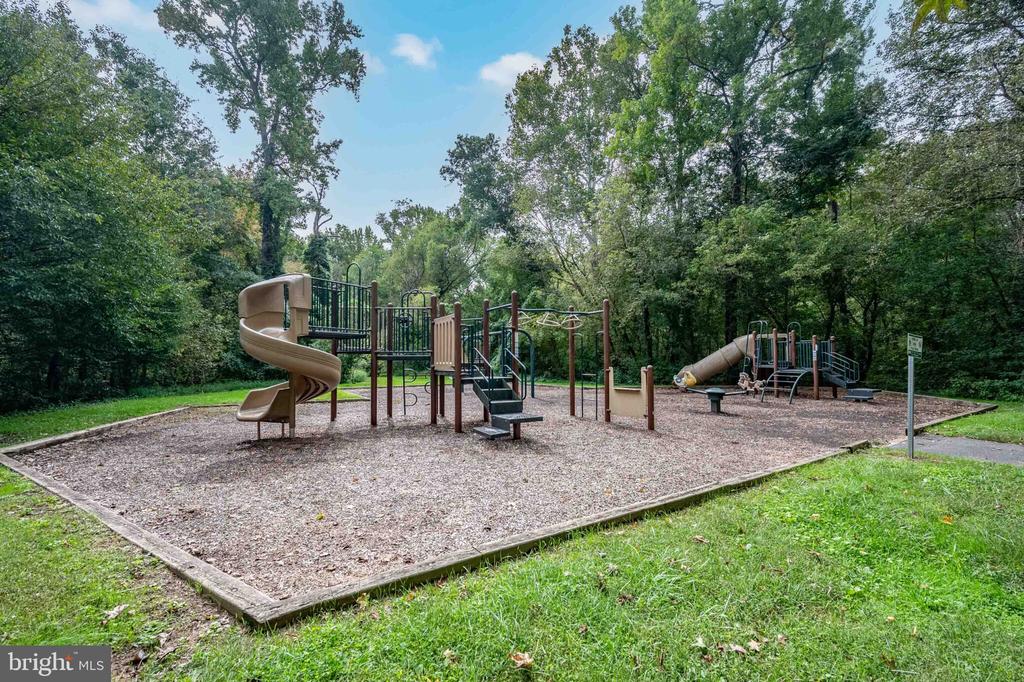 Outdoor playground with slides and climbing structures beneath mature trees.