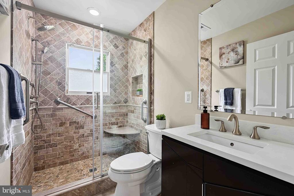 Bathroom with a tiled glass shower, pebble floor, toilet, and dark-wood vanity.