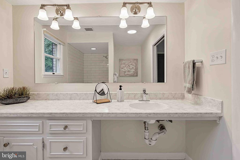 Bathroom vanity with a marble-look counter, large mirror, and reflected tiled shower.