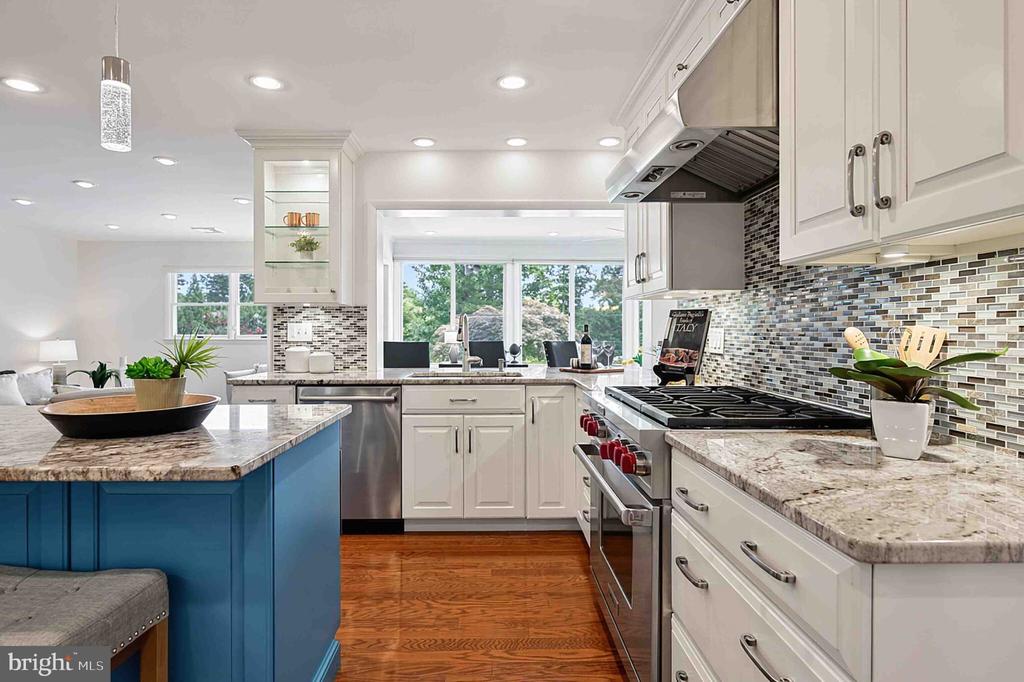 Kitchen with white cabinets, granite counters, a blue island, stainless steel appliances, and hardwood floors.