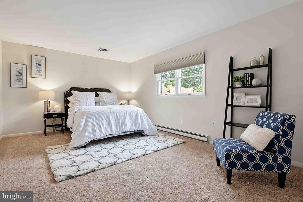 Bedroom with a white bed, patterned rug, and blue armchair beside a ladder bookshelf.